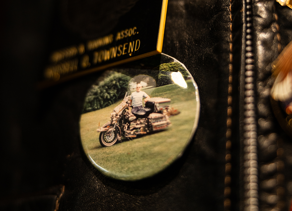 Round pin on a black leather vest displaying a photo of a person seated on a motorcycle on grass