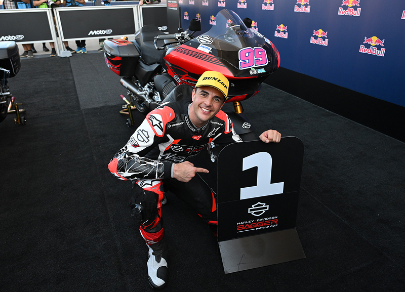 Motorcycle racer smiles beside his race bike while holding a first-place trophy in the paddock area
