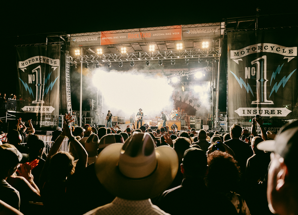 Wide shot of a concert stage at a motorcycle rally with performers under lights and a crowd watching.