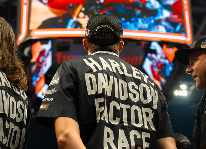 Harley-Davidson Racing team members watch a large arena screen showing a motorcycle race during Flat Out Friday
