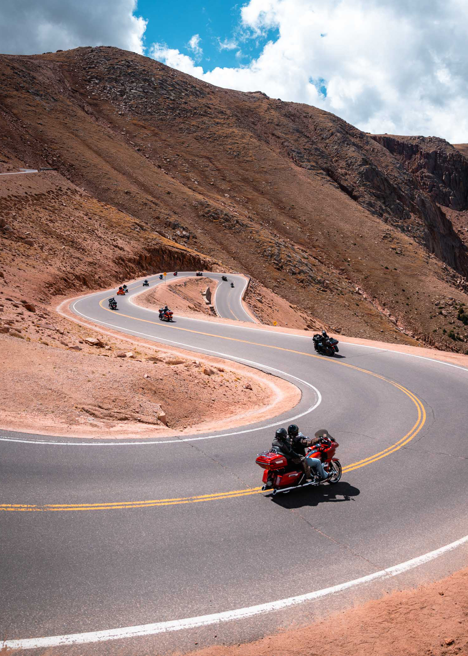 Motorcycles navigating sharp curves as they descend the road down Pikes Peak under a partly cloudy sky