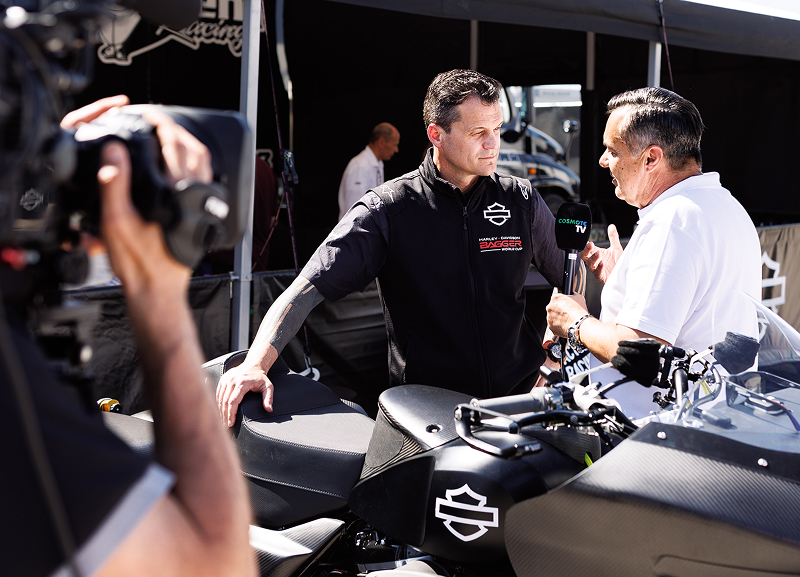 Harley-Davidson team member is interviewed by the media while standing next to a motorcycle in pit lane