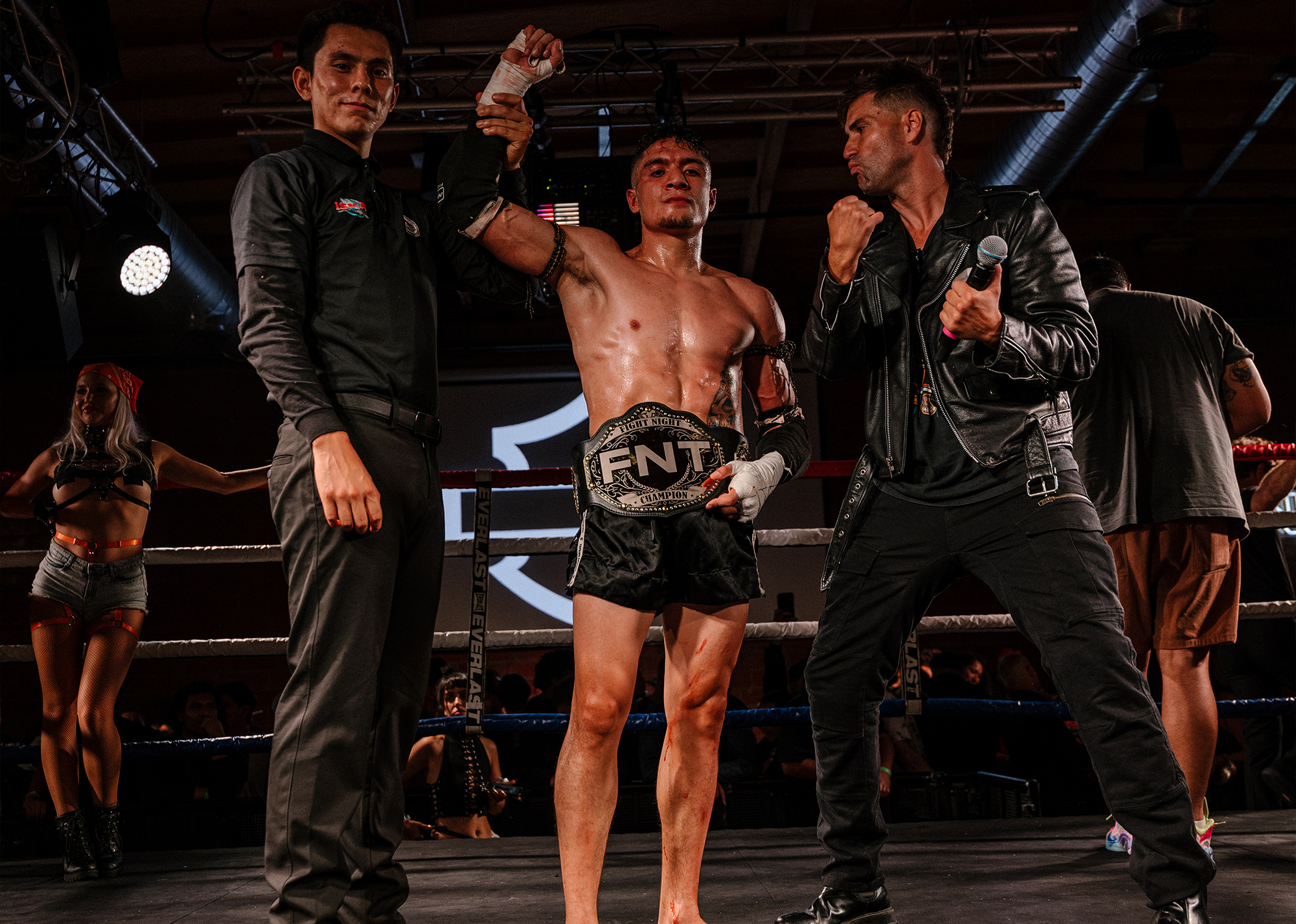 Referee raises fighter’s hand as he celebrates victory with FNT championship belt in the ring.