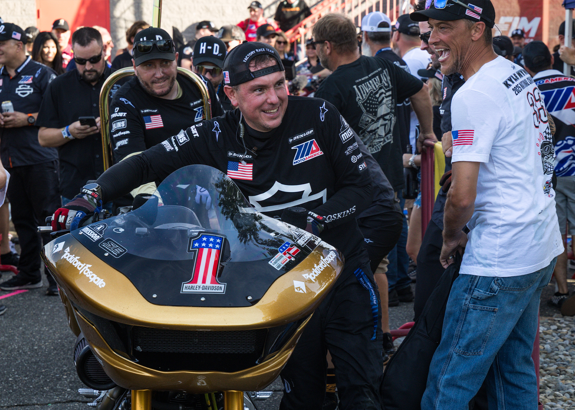 Harley-Davidson Factory Racing Chief Race Mechanic Dave Hopkinson pushes Kyle Wyman’s winning gold bike through cheering fans after a race.