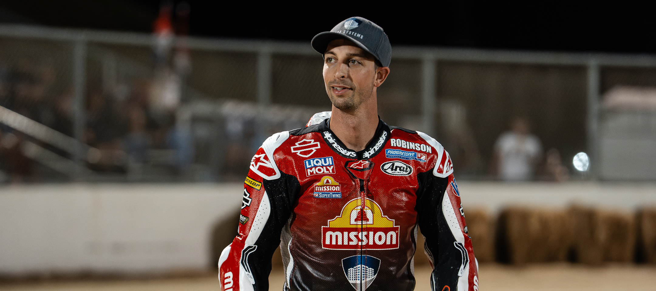 Brandon Robinson in red-and-black leathers stands trackside under stadium lights following a flat track event