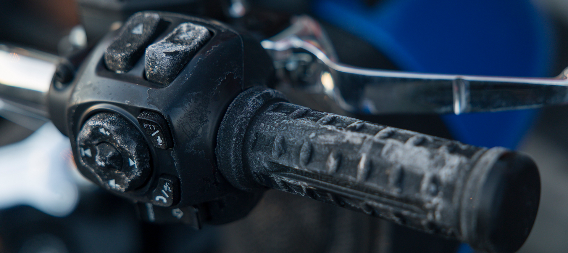Close-up of a motorcycle handlebar and control buttons covered in frost, showing icy texture on the grip