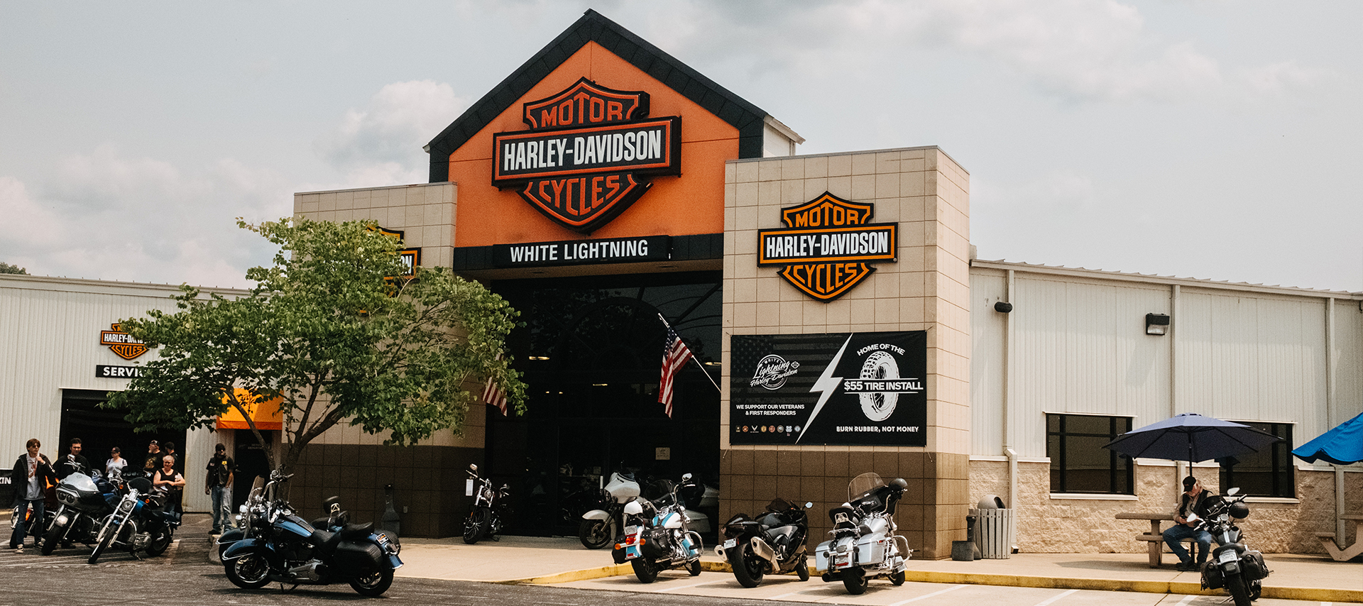 Parked motorcycles and riders outside of the entrance to White Lightning Harley-Davidson.
