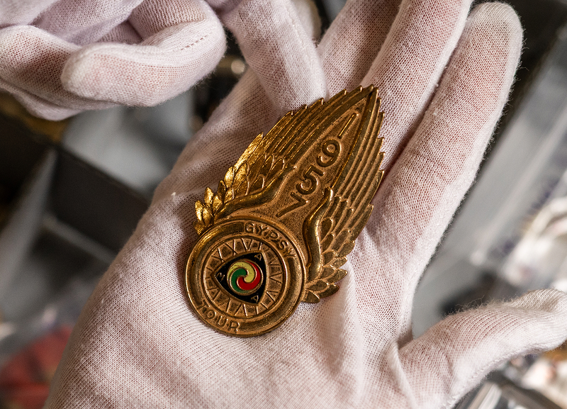 Gold winged motorcycle AMA emblem for the 1957 Gypsy Tour with circular center held in gloved hands over archival storage box