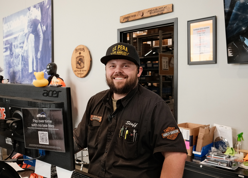 Dealership employee seated at front desk workstation with Harley-Davidson branding and displays nearby
