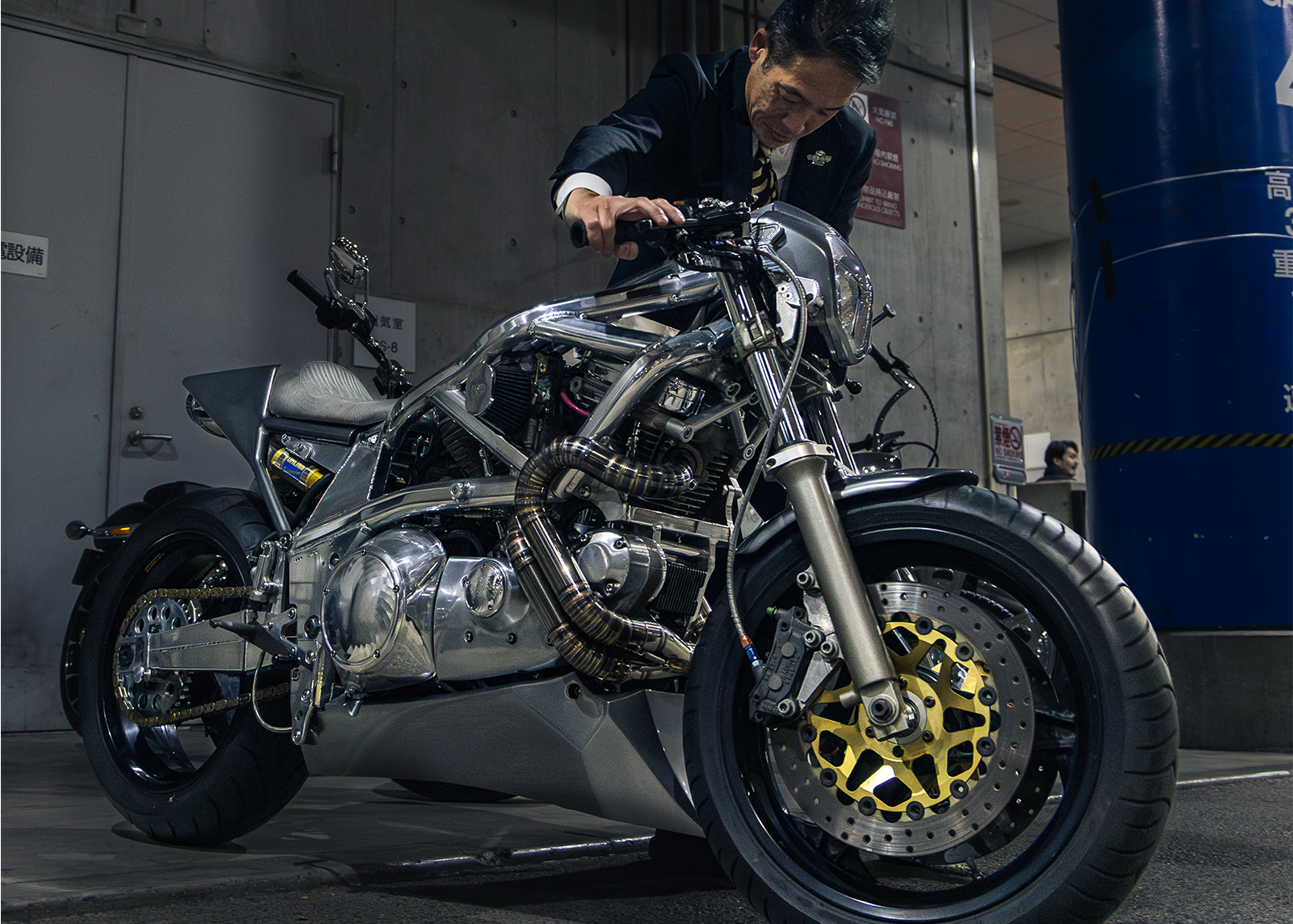 A custom motorcycle with a polished metal frame, exposed engine components, and gold brake rotors being staged for display