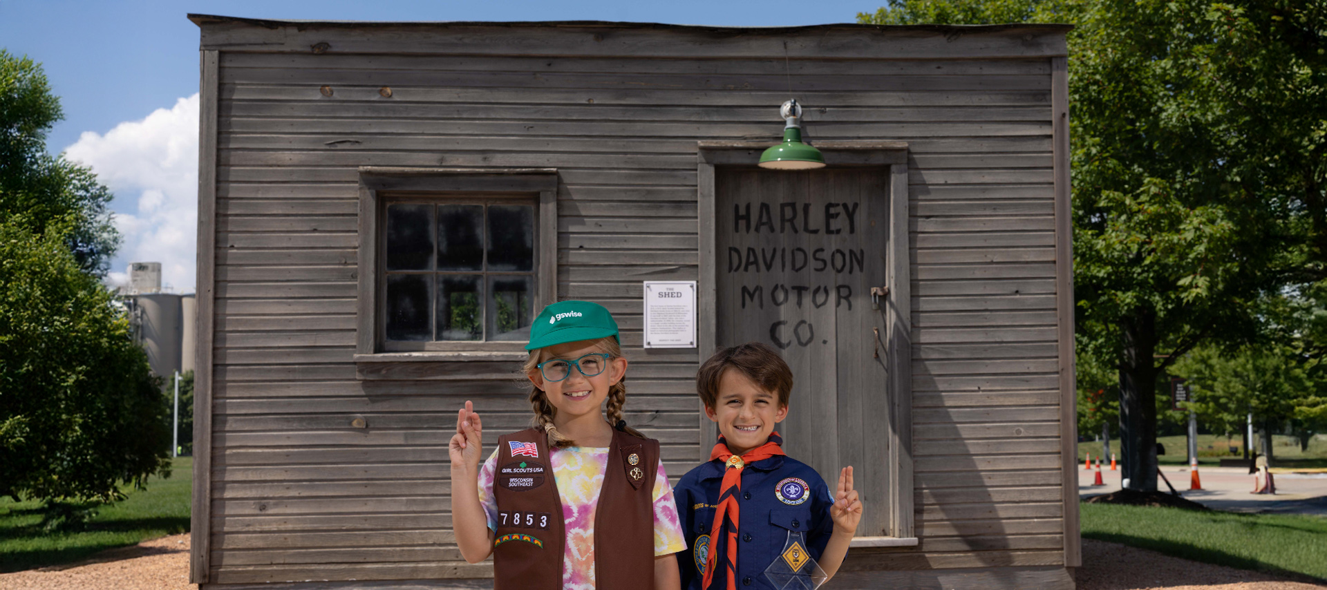 Two children in scout uniforms posing in front of Harley-Davidson Motor Co. building