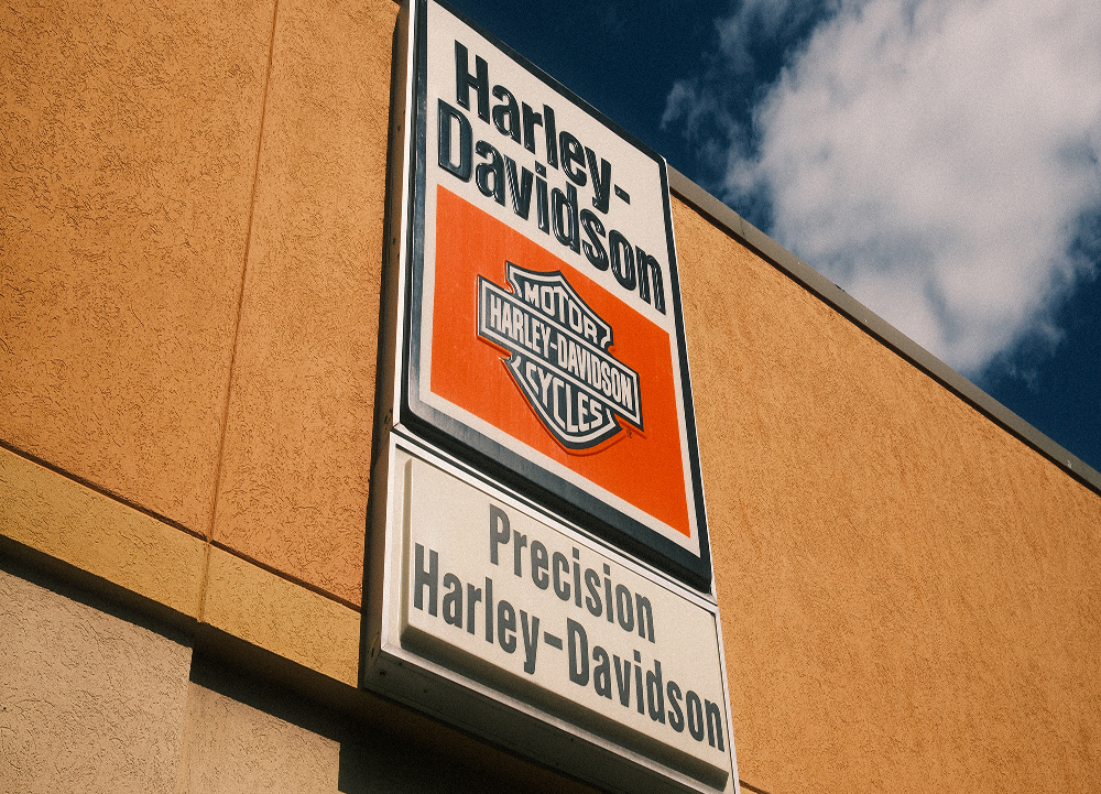 Looking up at a Precision Harley-Davidson vintage dealership sign mounted on tan building with blue sky background