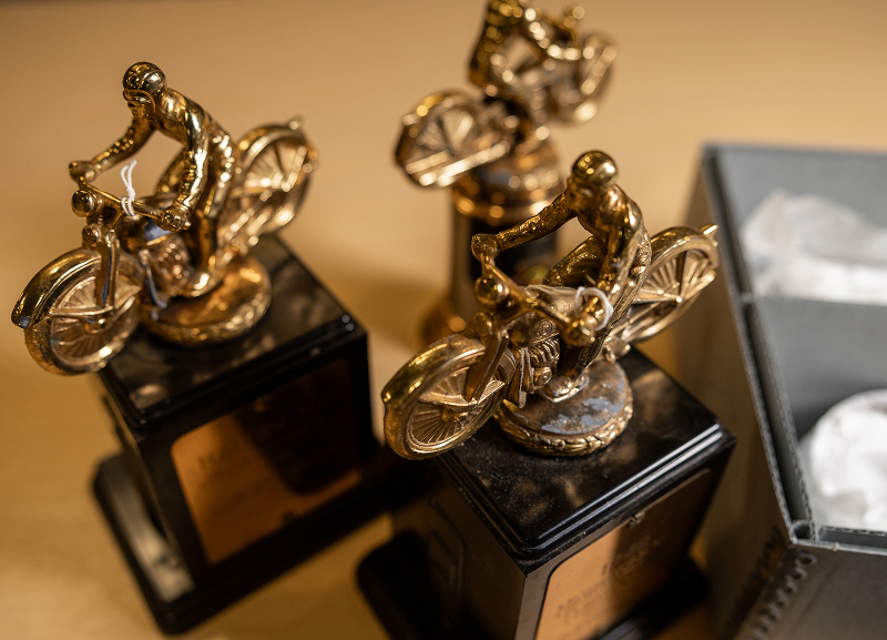 Three gold motorcycle trophies on black bases displayed beside an open box lined with tissue paper