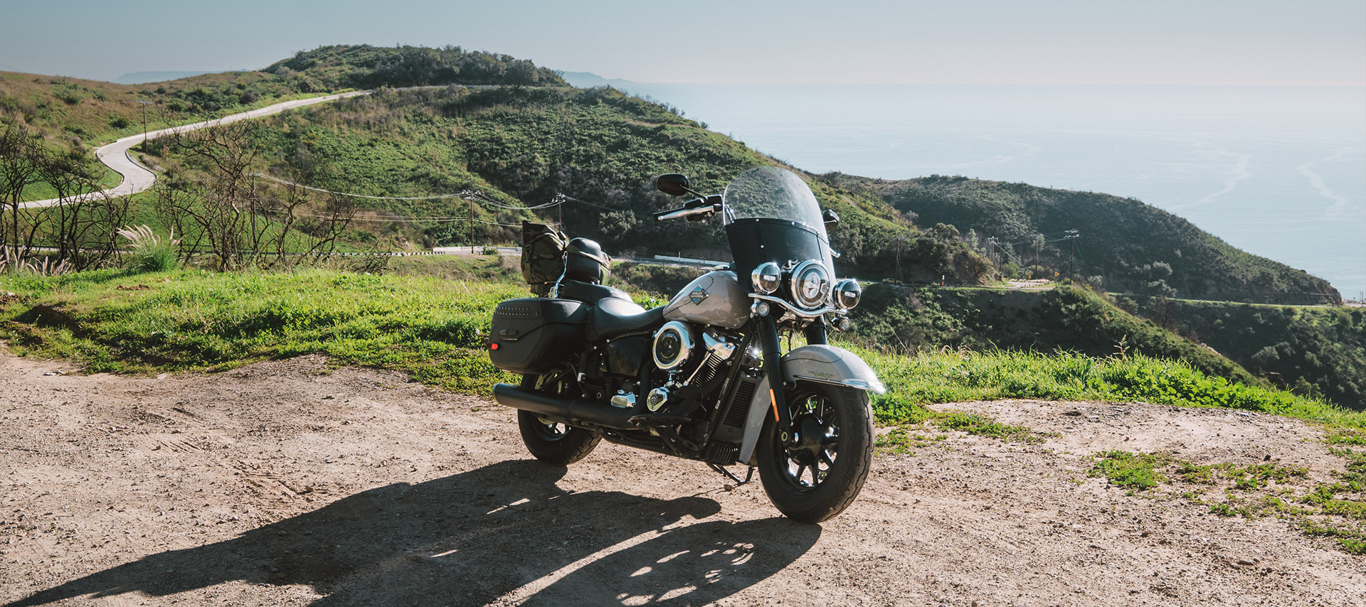 The author’s Harley-Davidson Heritage Classic parked on a roadside turnout with green hills, the ocean, and a winding road in the background