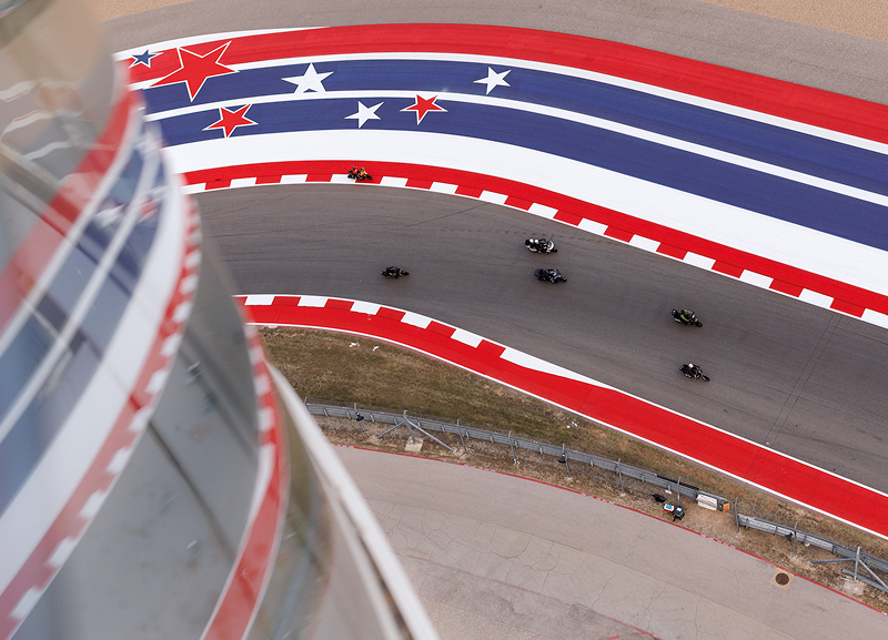 Aerial view of motorcycle racers leaning through a sweeping turn on a red white and blue racetrack