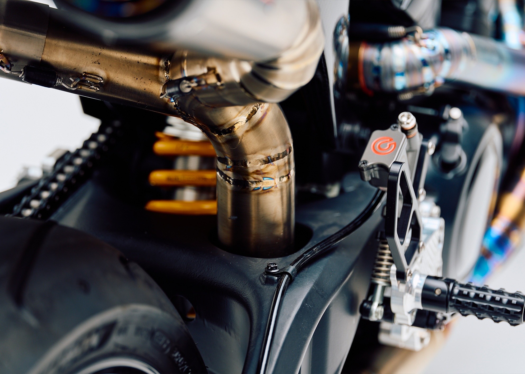 Close-up of the custom Pan America ST’s exhaust welds, Brembo rear brake master cylinder, and Öhlins rear suspension.