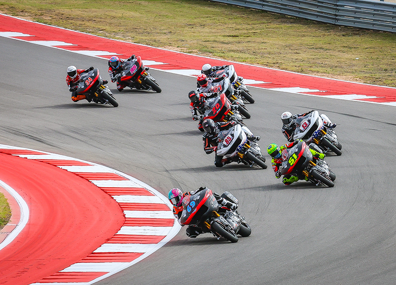 Group of motorcycle racers tightly packed as they lean through a sharp corner on a professional road course