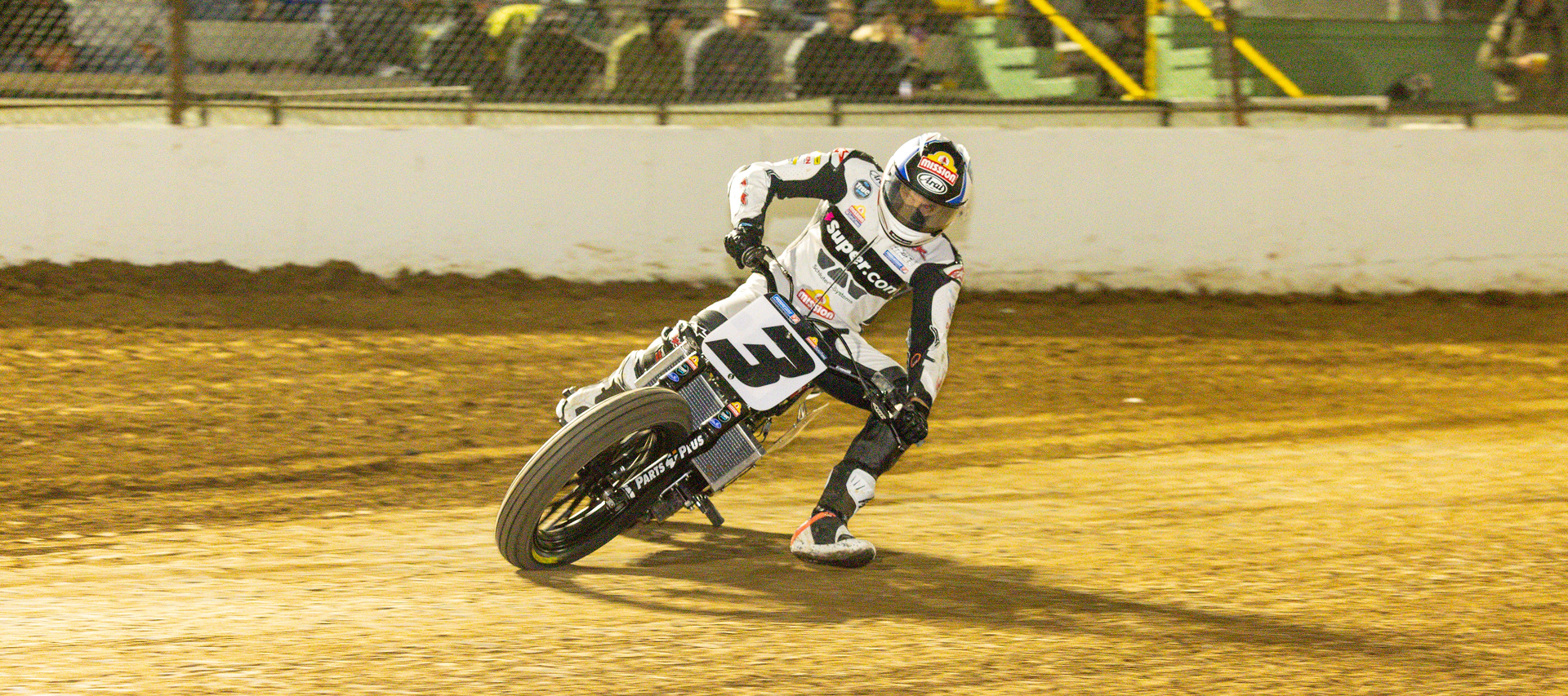 Rider Briar Bauman on a flat track motorcycle slides through a dirt corner under stadium lights during a nighttime race
