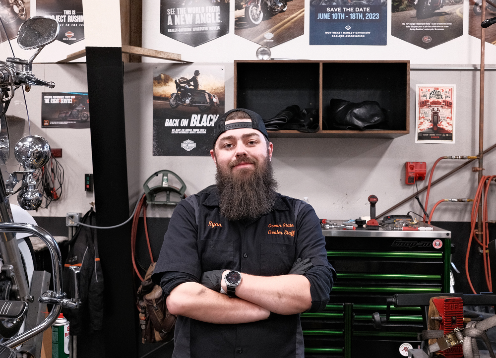 Harley-Davidson technician standing in service bay with tools, posters, and workbench behind them