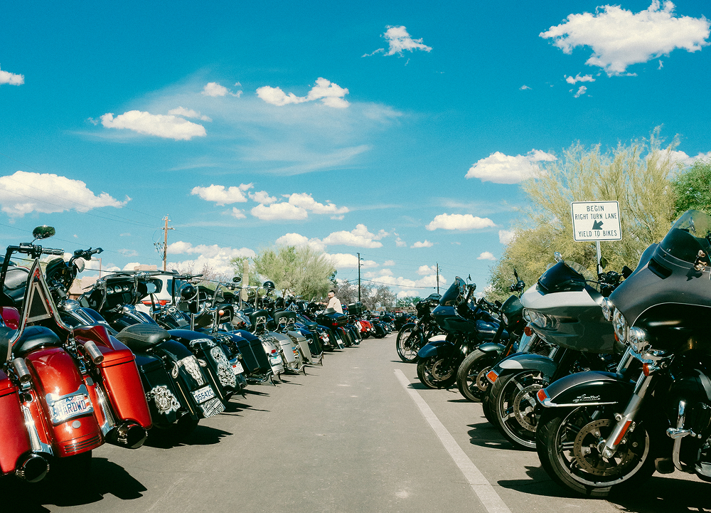 Long row of parked motorcycles lined along a street under a bright blue sky at a large outdoor ride event.