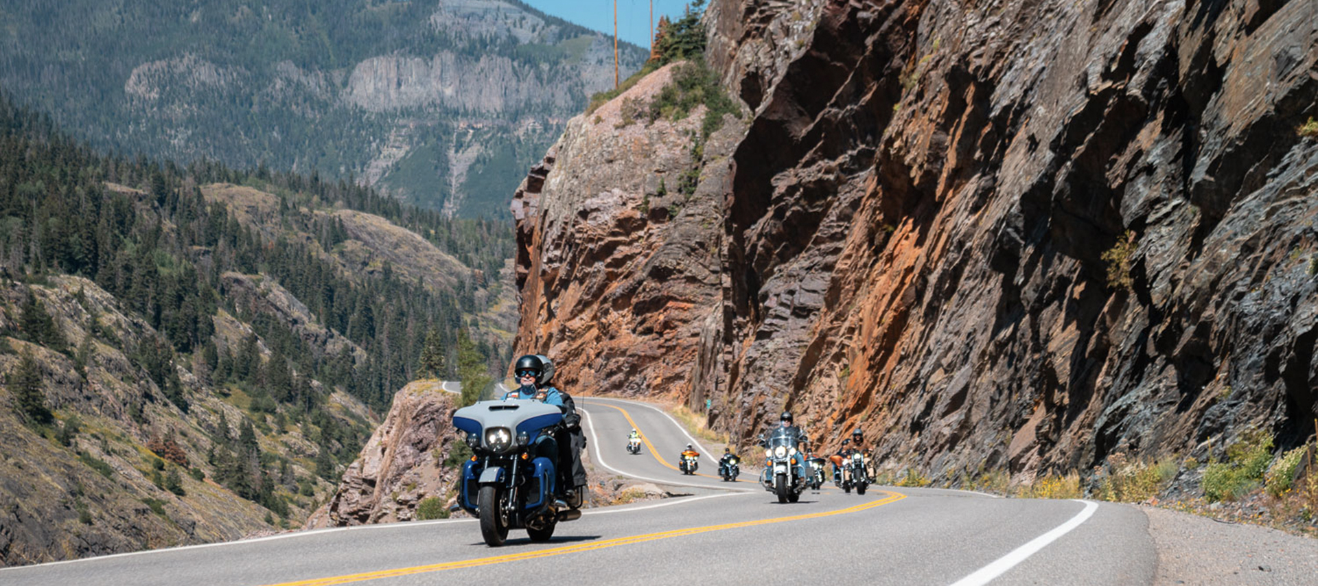 Pacific Coast HOG Chapter poses for a photo in front of mountains with their chapter flags