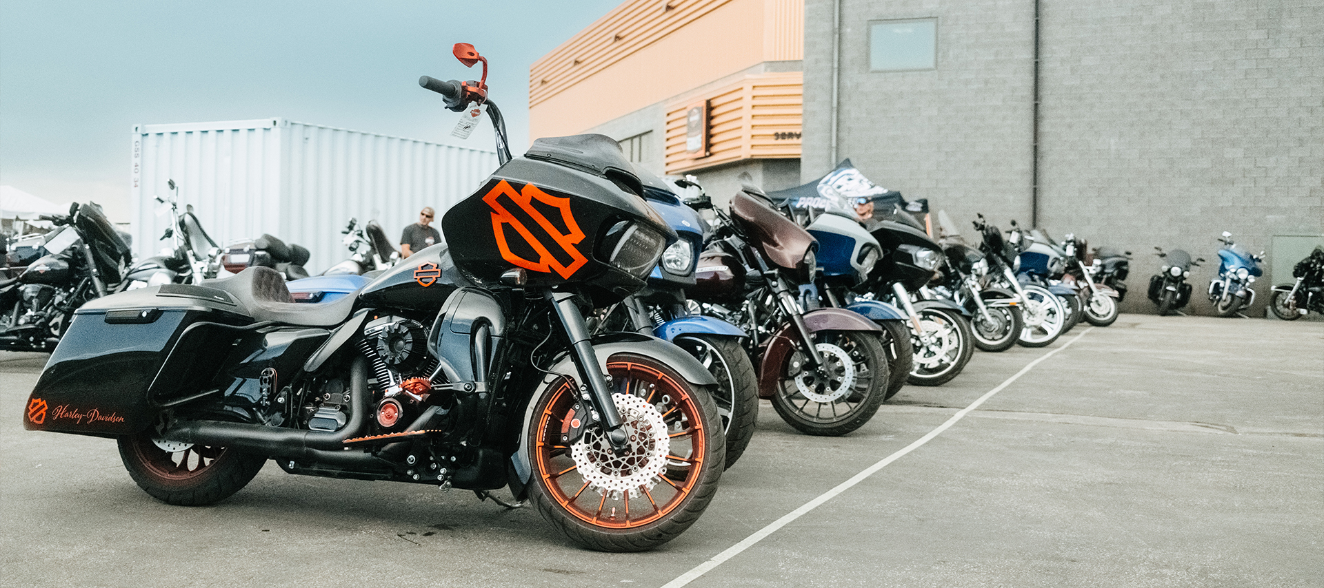 Line of Harley-Davidson touring motorcycles parked, with a black bike featuring bold orange accents in front.
