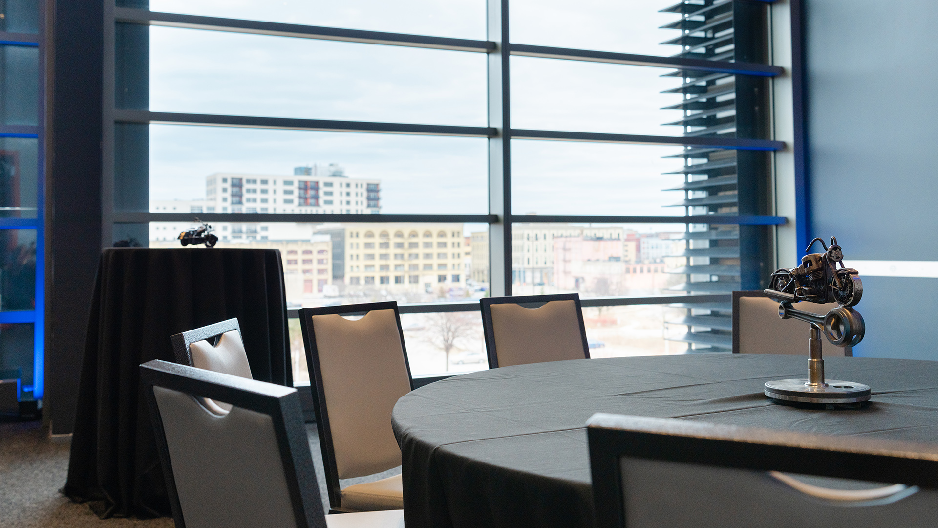 Event tables with black linens, miniature motorcycle centerpiece and city view through large window panels