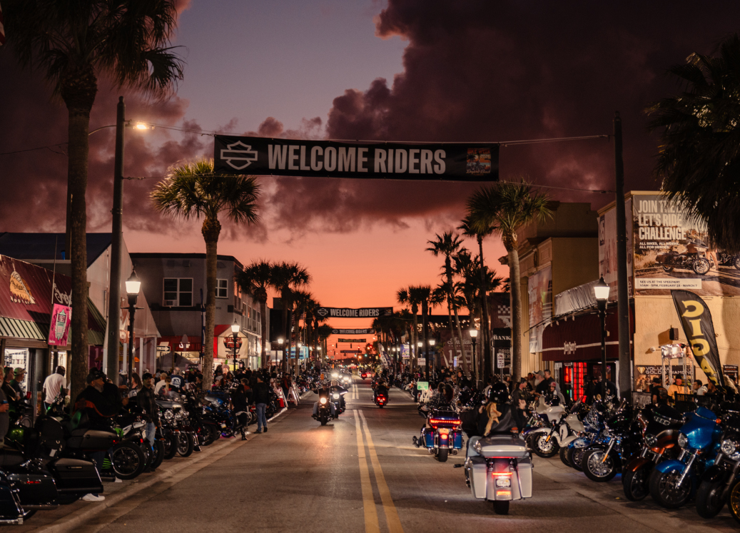 Daytona Beach Main Street at sunset, crowded with motorcycles under a Welcome Riders banner