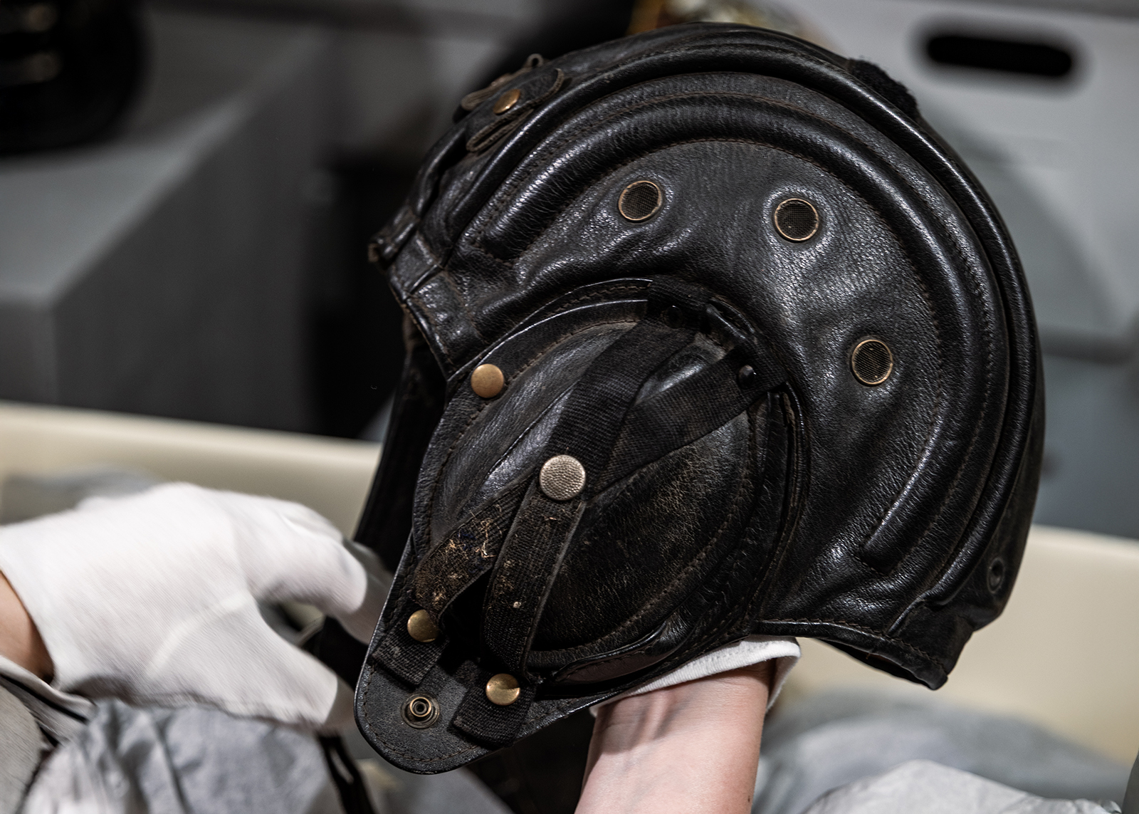 A museum archivist holds a vintage leather aviation style motorcycle helmet.