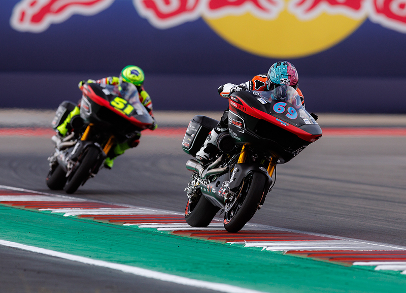 Two motorcycle racers exit a corner, tires near curbing on a professional road course