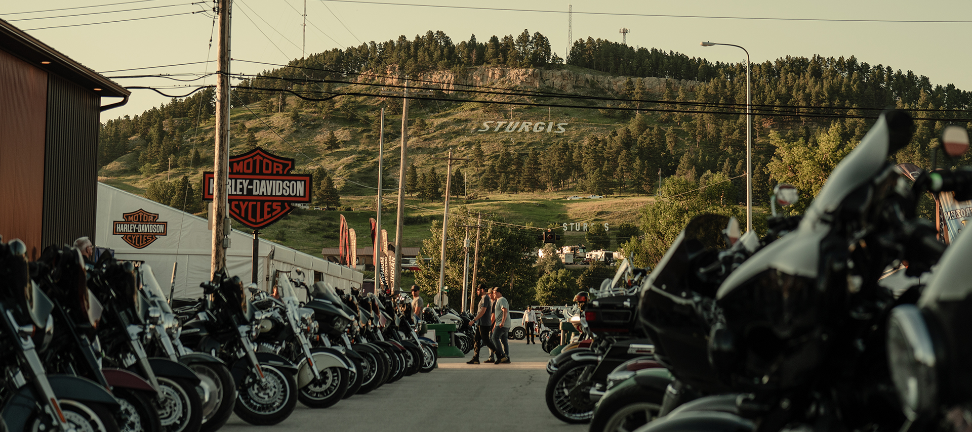  Rows of Harley-Davidson motorcycles lined up in Sturgis with hillside sign in the background.