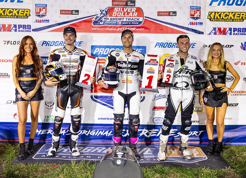 Podium finishers stand with helmets and place markers before sponsor backdrop at flat track race ceremony