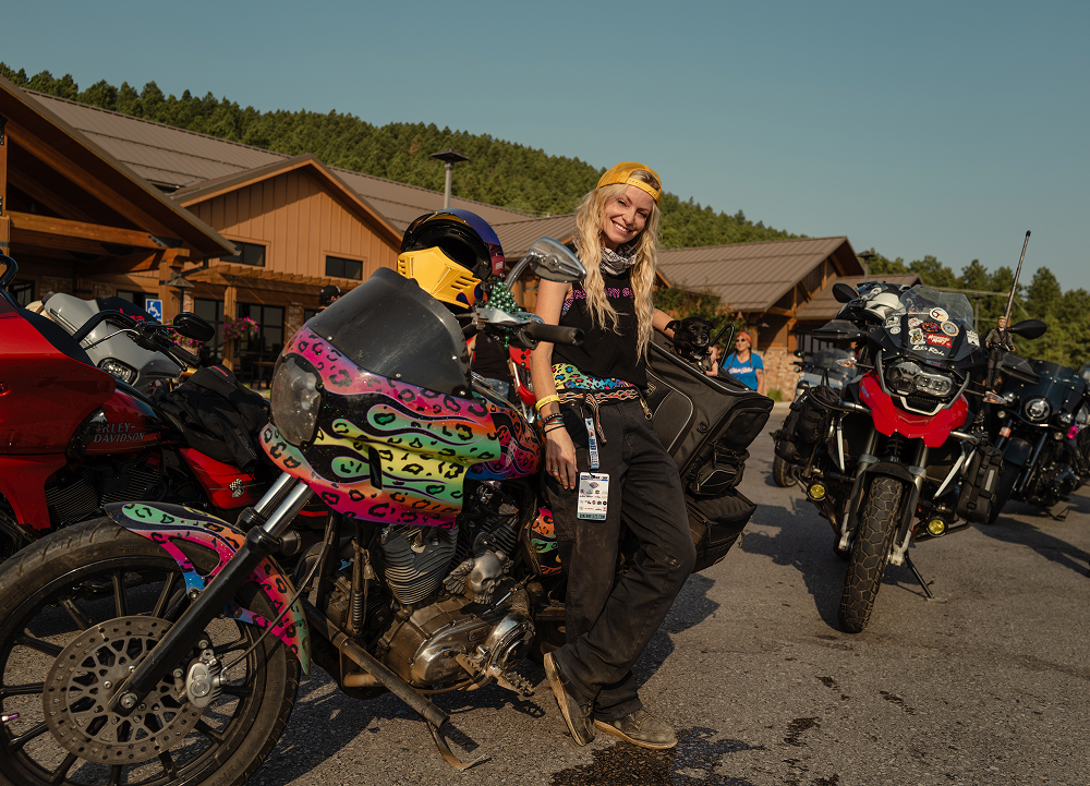 Rider poses beside a brightly painted custom motorcycle among a row of bikes at a Sturgis rally venue