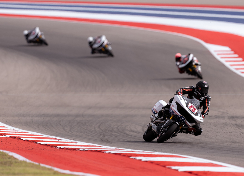 A group of riders navigate a wide S curve on a striped racetrack