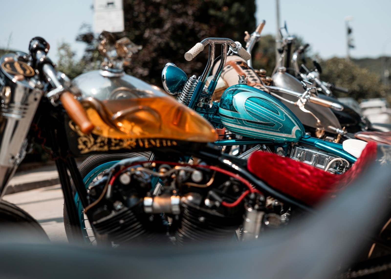 Close-up view of customised motorcycle tanks, seats, and handlebars at an outdoor bike event.