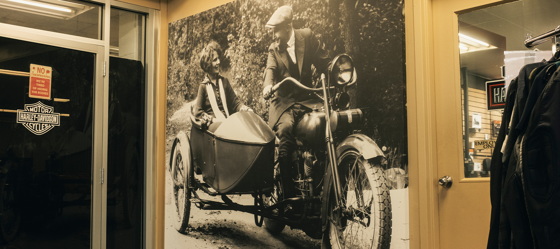 Vintage wall mural of a man riding a Harley-Davidson with a woman in a sidecar inside the Woodstock Harley-Davidson dealership.