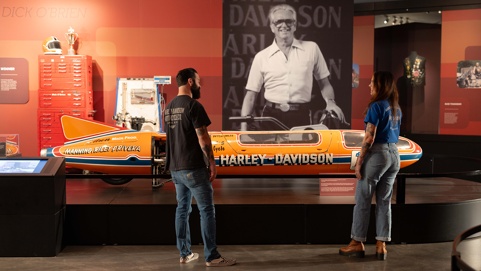 Two visitors exploring Harley-Davidson streamliner display