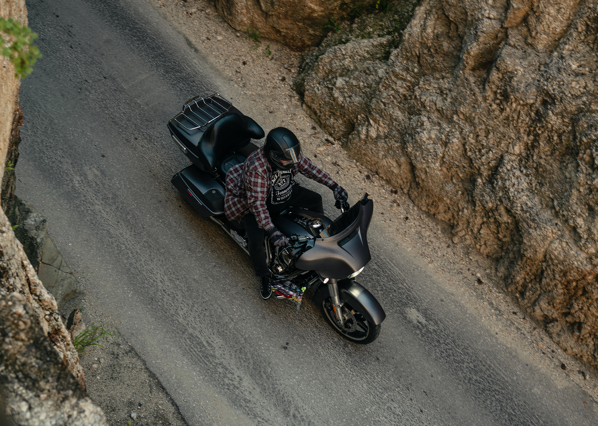 Motorcyclist in plaid shirt rides through narrow rock passage, viewed from above.