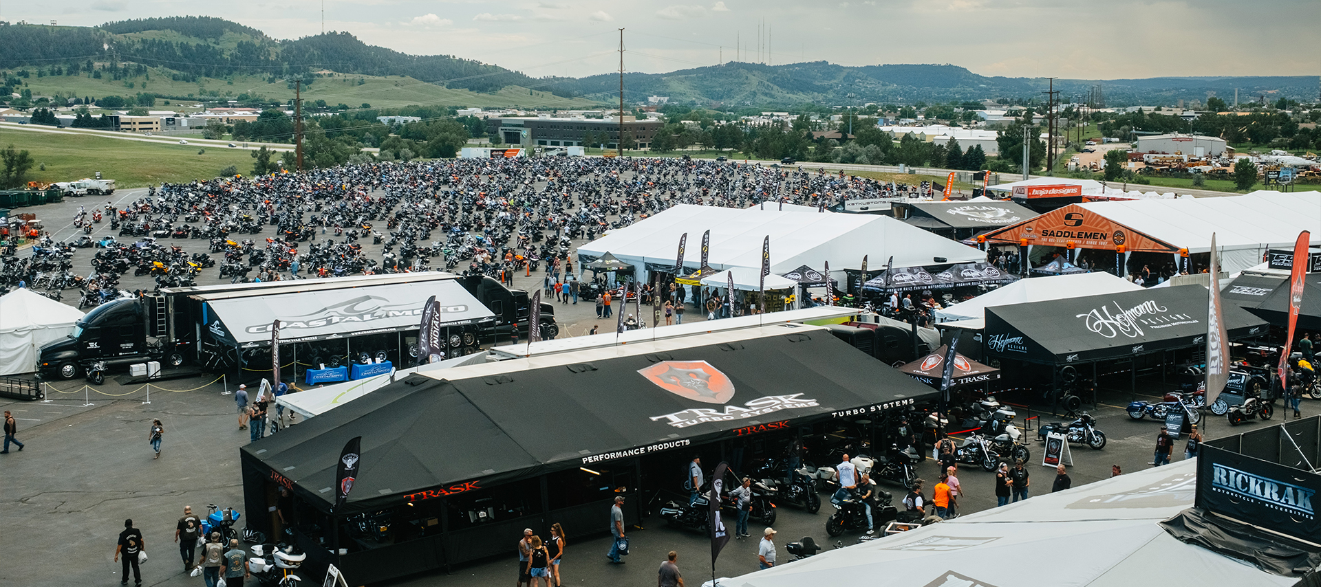Aerial view of the massive Exit 15 motorcycle rally at Black Hills Harley-Davidson with vendor tents, bikes, and crowds filling the lot.