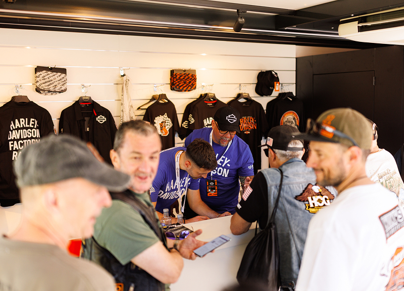 Harley-Davidson enthusiasts line up inside a merchandise display, shopping for apparel and gear