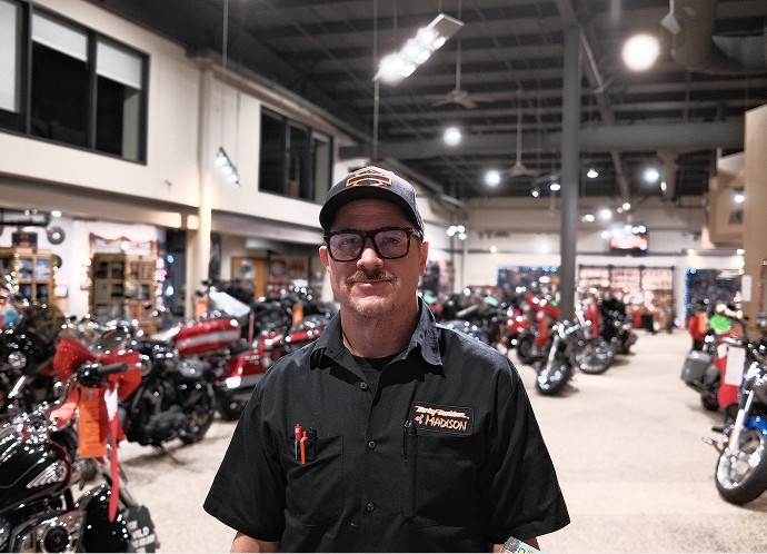 Employee standing inside a Harley‑Davidson showroom, with rows of motorcycles and bright overhead lighting in the background