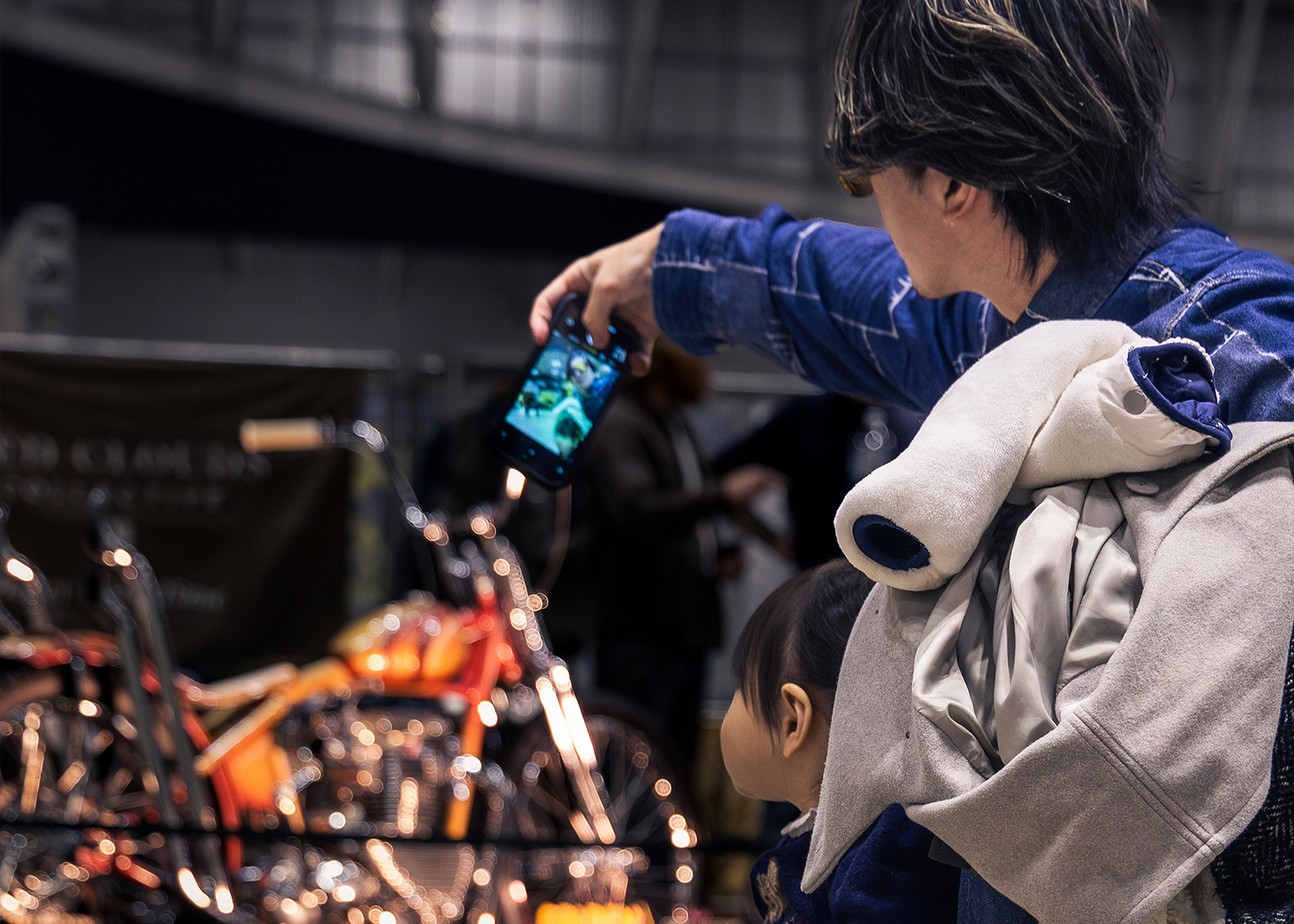  A father takes a photo with his cell phone of a custom motorcycle with his young daughter by his side