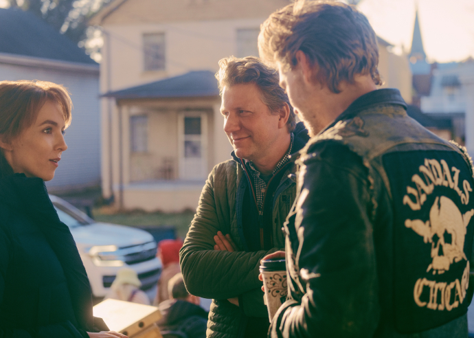 Austin Butler staring as Benny drinks his coffee as his talks with two people