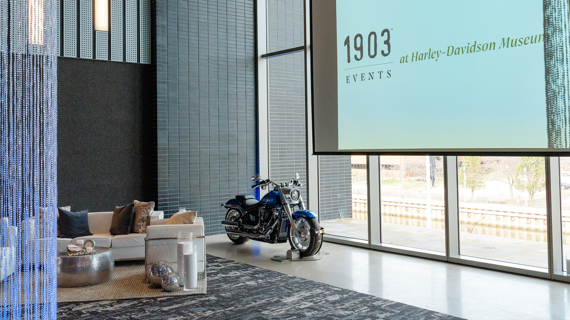 Harley-Davidson event space with lounge seating, motorcycle display, and large screen