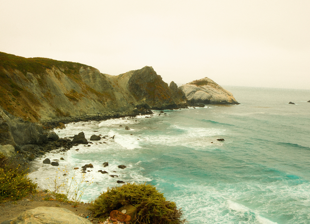 Rocky coastline and turquoise ocean viewed from a cliffside overlook along a rugged coastal route
