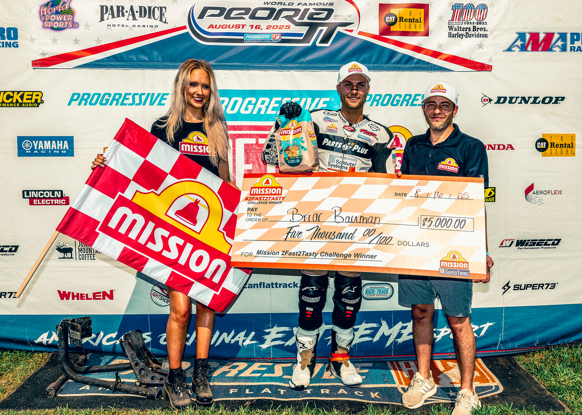 Standing in front of a banner with sponsor logos Briar Bauman accepts an oversized check after winning a flat track event