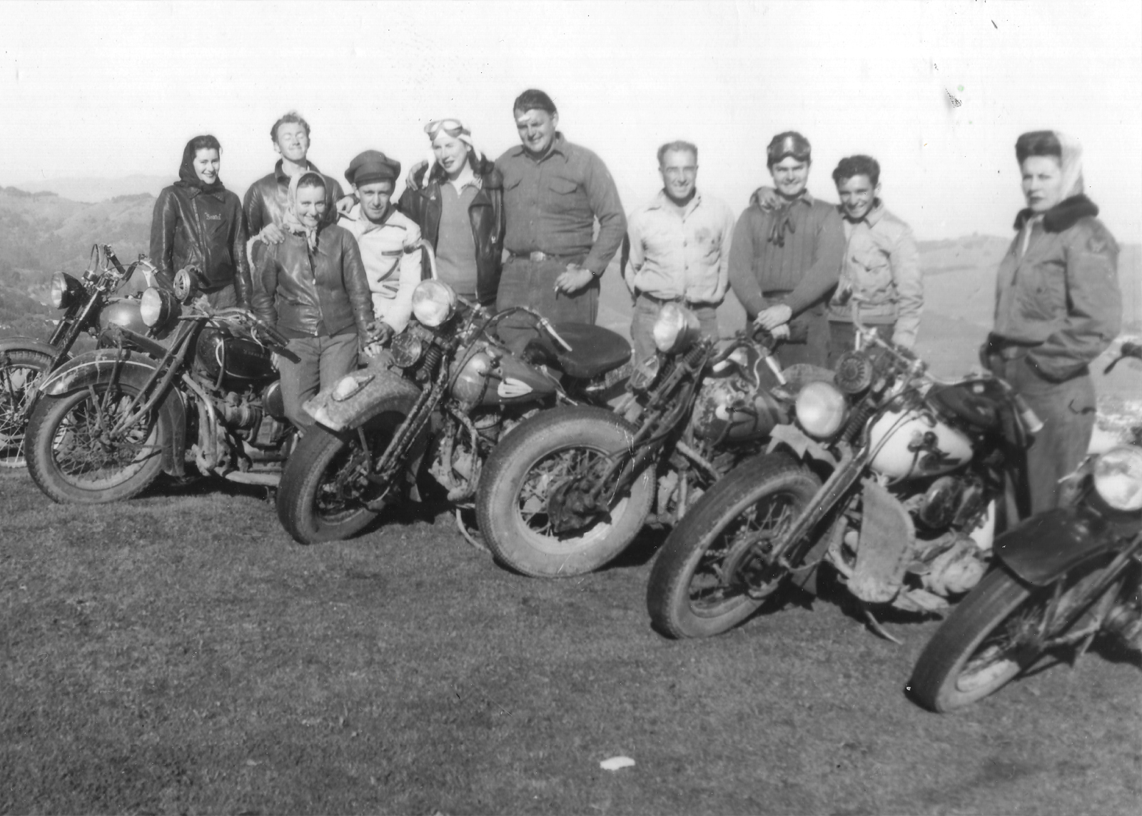 A group of people pose behind a line of motorcycles