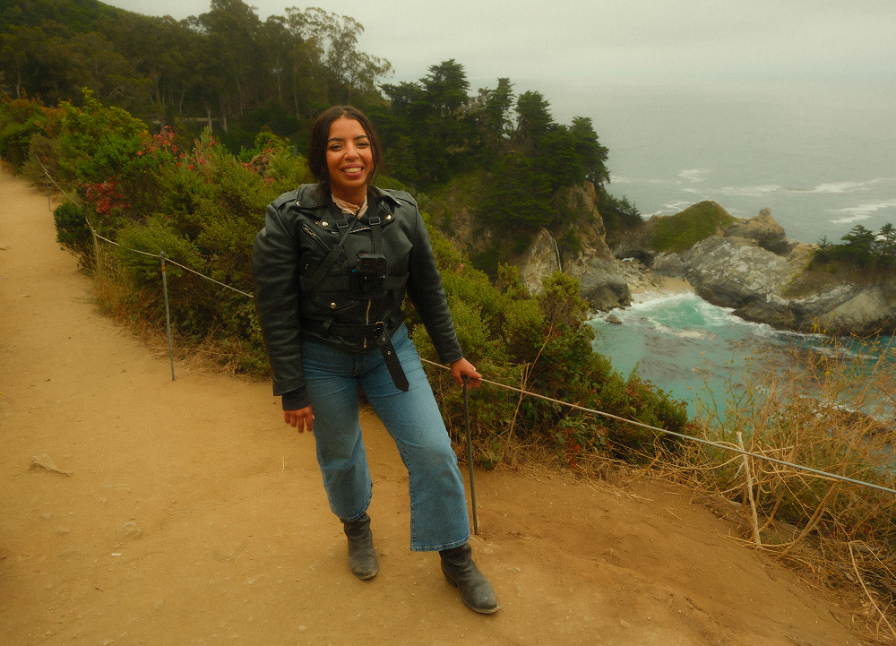 The author standing at a coastal overlook with ocean cliffs, rocky shoreline, and crashing waves below