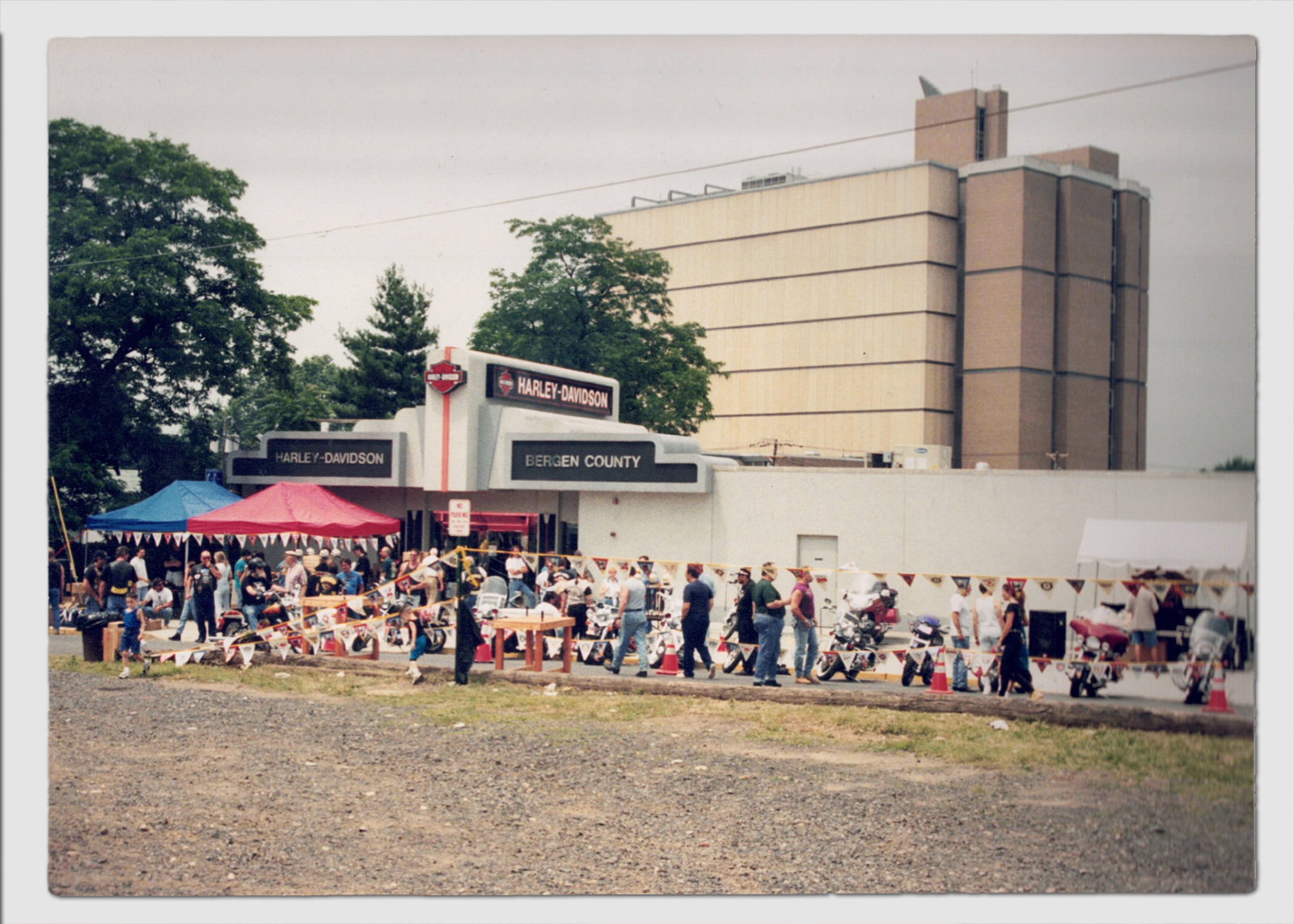 Vintage photo of an outdoor crowd gathered at an early Harley-Davidson Bergen County dealership with tents and signage.