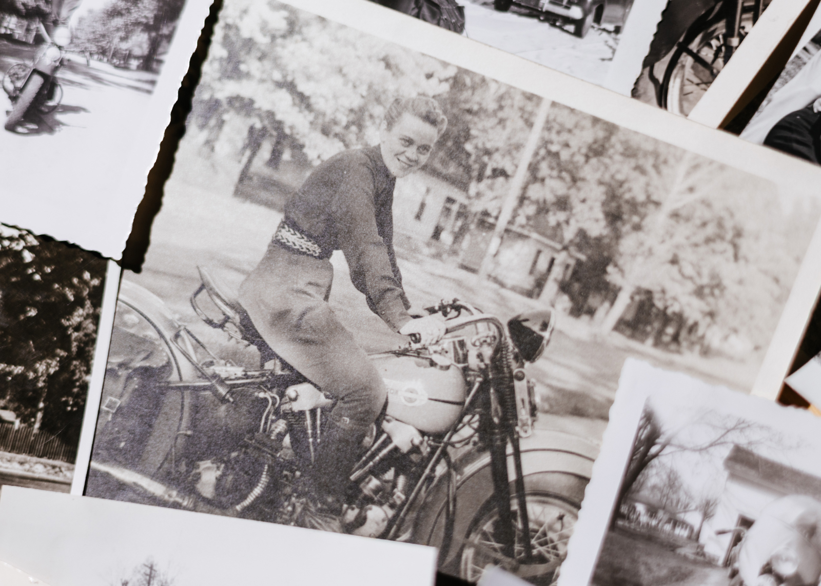 A photo of a vintage Motor Maid photo showing a woman sitting on her motorcycle and smiling at the camera.